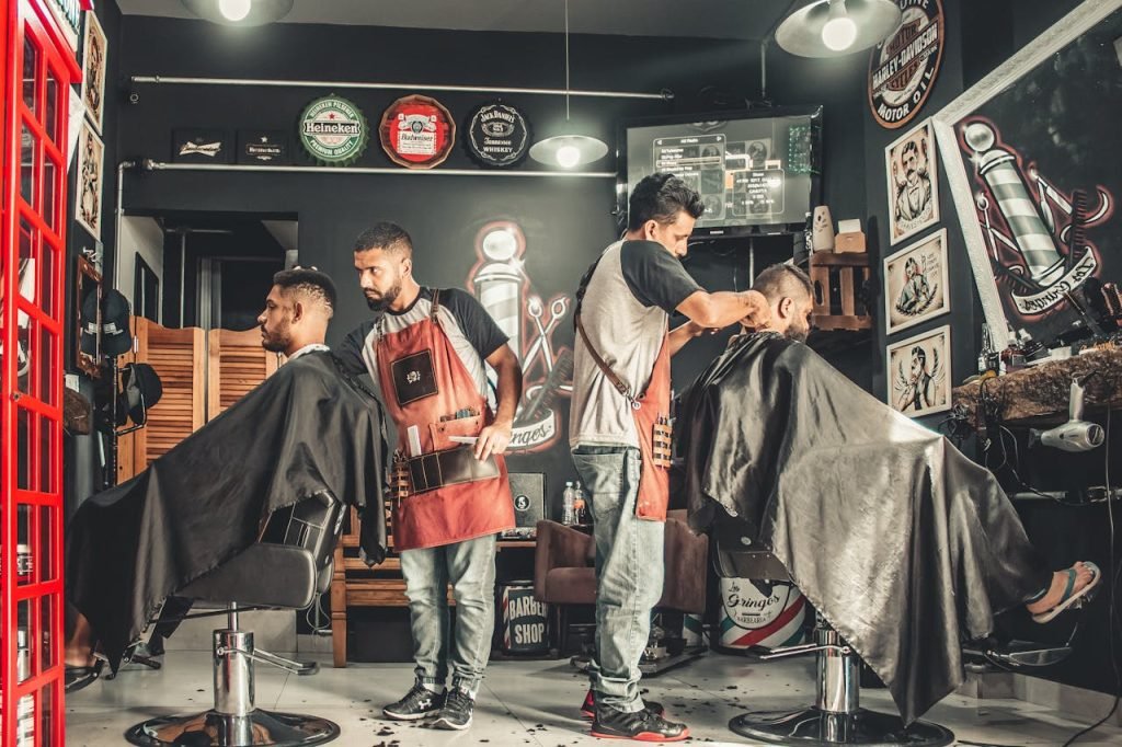 Servicios. A bustling barbershop with two men getting haircuts, showcasing a vibrant barber environment.