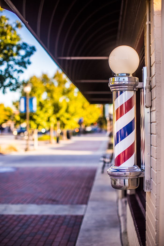 Barberia Unisex Cesar. Classic barber pole on a vibrant city street under a sunny sky.